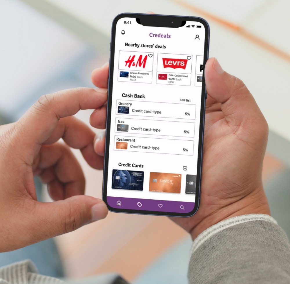 A phone held in both hands showing the Credeals app: nearby store deals, cash-back categories, and a row of saved credit cards.