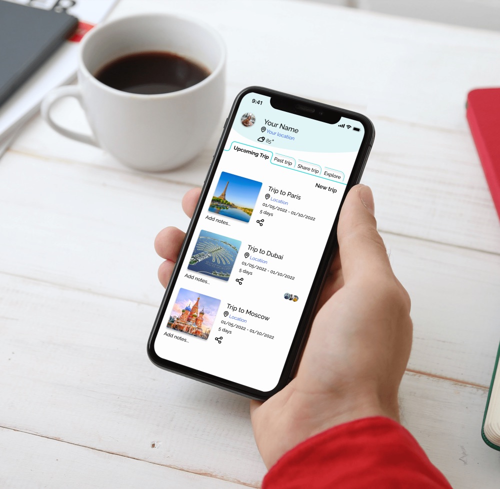 A phone held above a desk showing the Tripland app: a profile header and a list of upcoming trips to Paris, Dubai and Moscow with dates and durations.